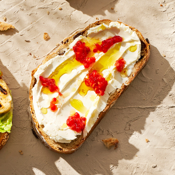 Rustic bread toast with white spread, yellow fruit, and red jam on a beige textured background