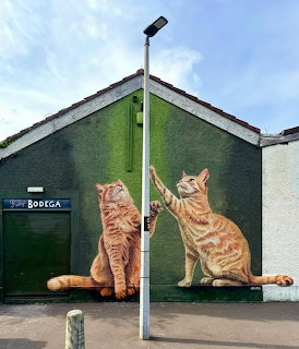 Street art mural of two orange tabby cats on green wall beside building