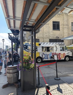 Food truck parked outside brick brewery building with covered patio and visitors