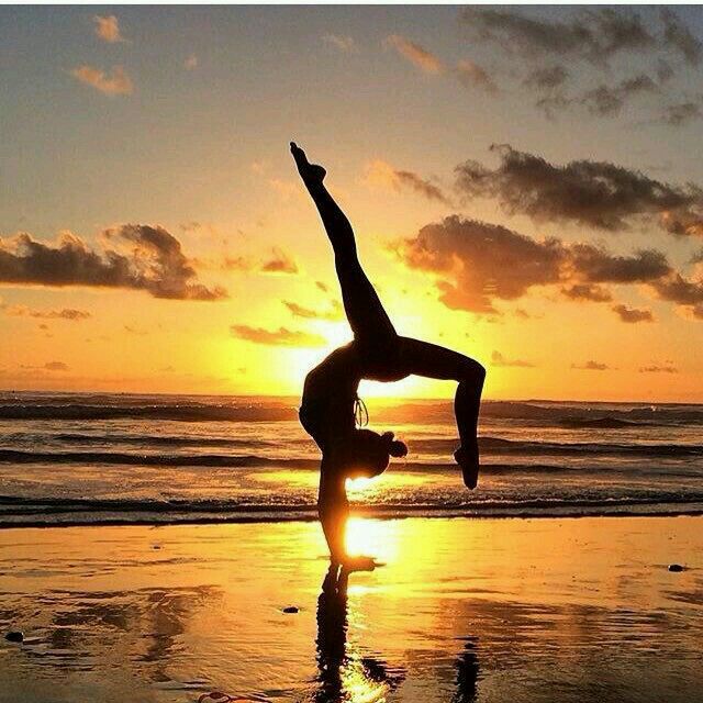 Silhouette of person doing yoga backbend on beach at sunset with ocean and golden sky