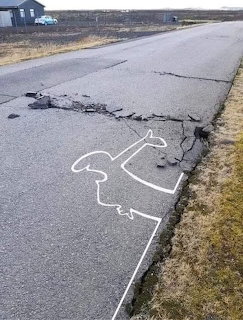 Cracked asphalt road with broken edge and a white outline marking the damaged area
