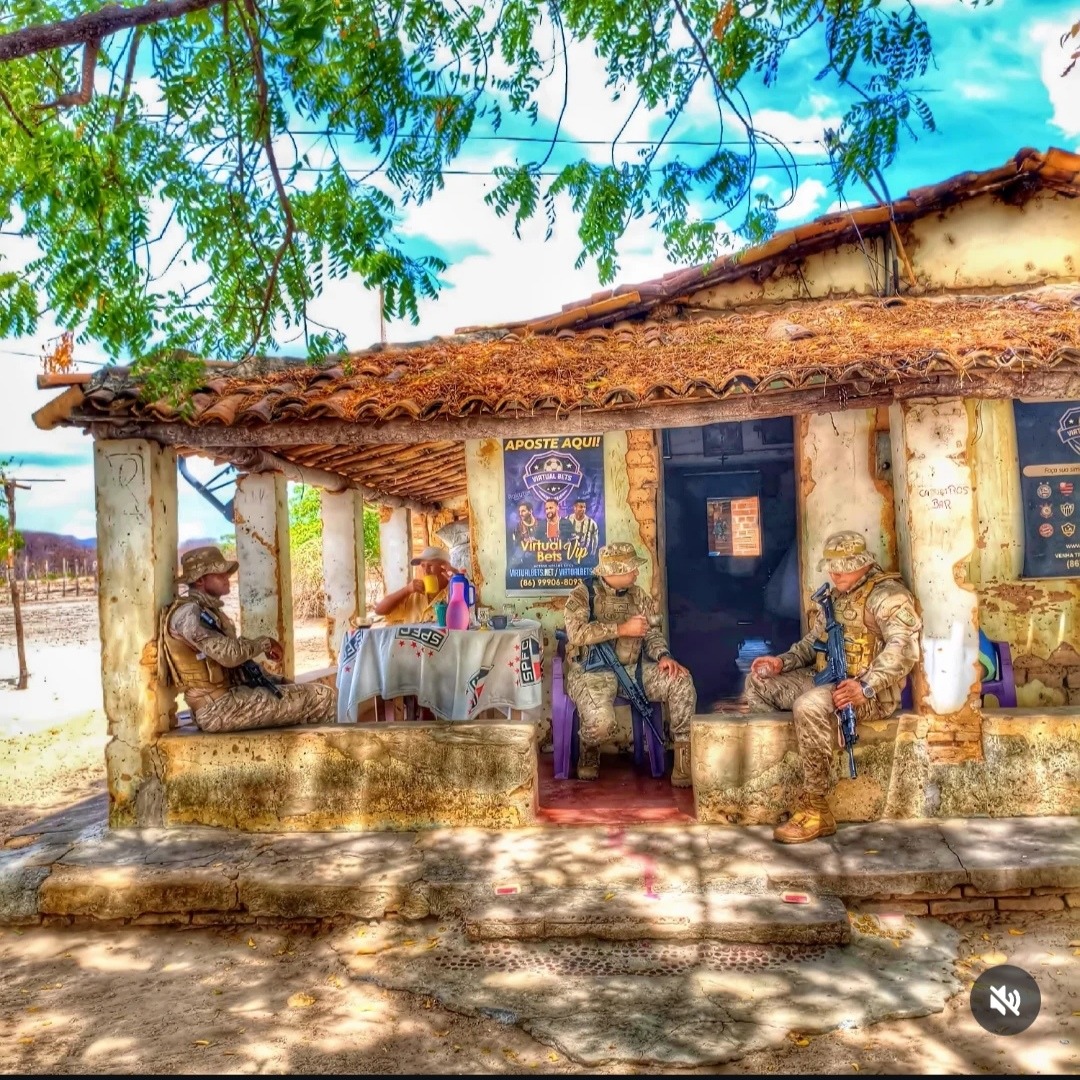Rustic village house with thatched roof, stone bench, and trees casting shade on sunny day