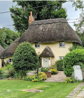 Yellow cottage with thatched roof, garden path, and flowering plants in front yard