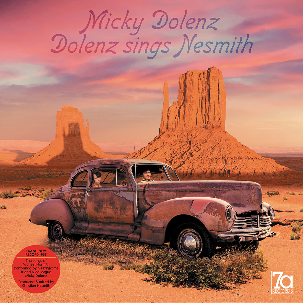 Rusty vintage car in a desert with tall rock buttes and a pink sunset sky