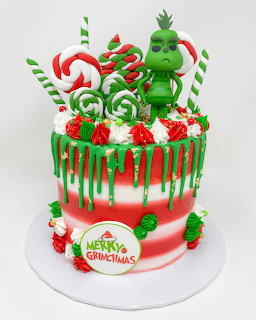 Christmas cake with Grinch topper, candy canes, lollipops, and red drip icing