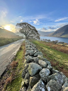 Stone wall beside rural road with lake and mountains in background