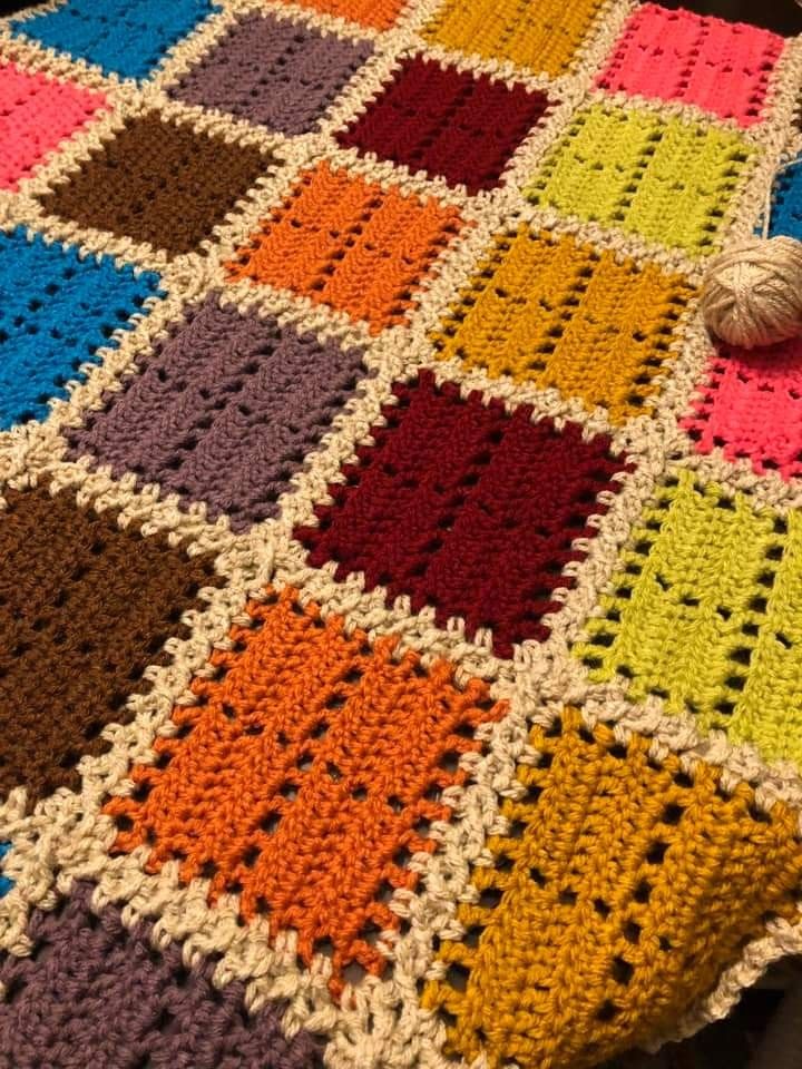 Colorful crochet granny square blanket with multicolored squares and cream borders on carpet