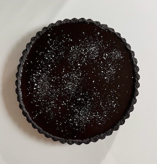 Round chocolate tart dusted with sugar in a fluted tart pan viewed from above
