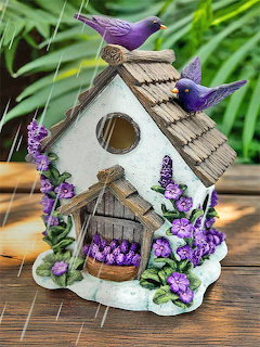 Decorative birdhouse with two purple birds and violet flowers on a wooden table