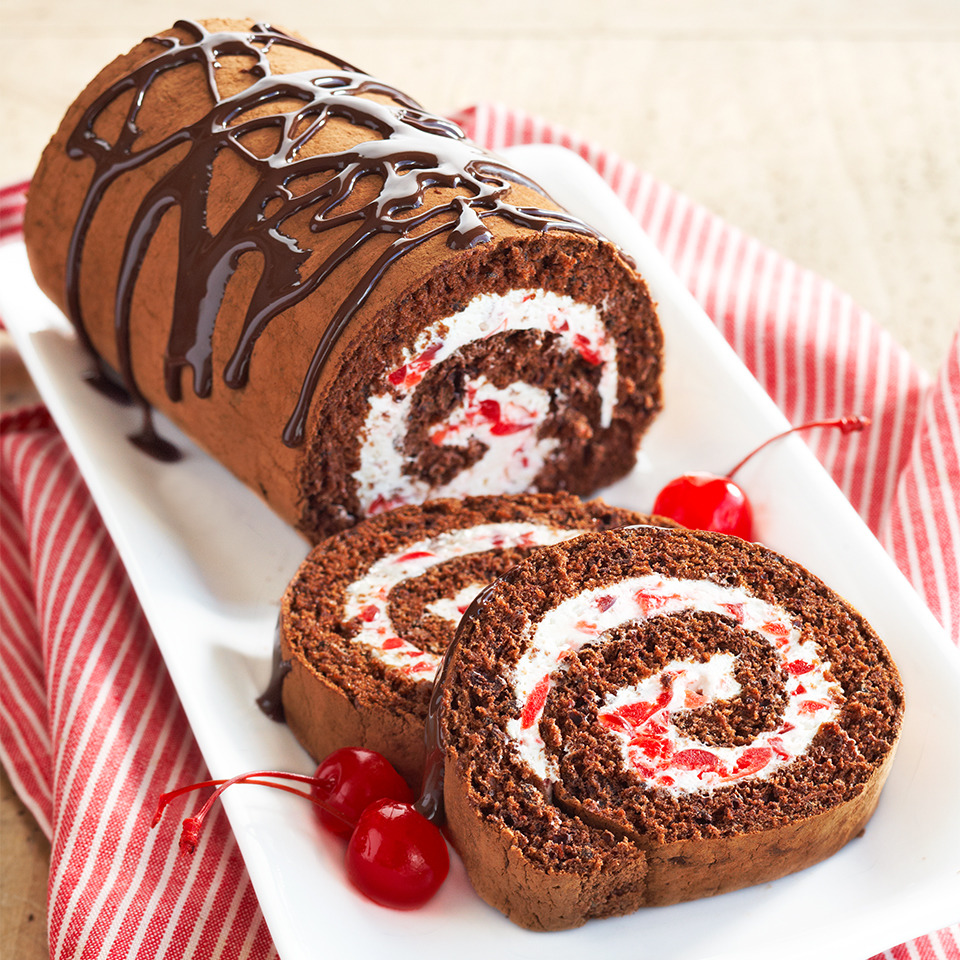 Sliced chocolate roll cake with cream and cherry filling on white plate