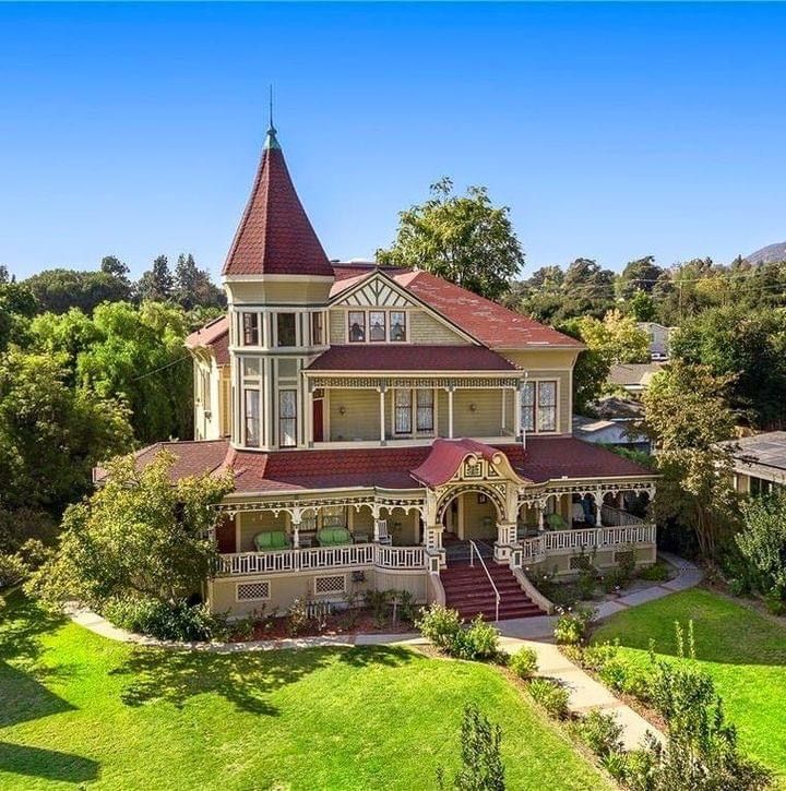 Victorian house with red turret and wraparound porch on green lawn