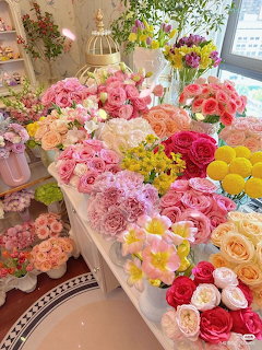 Bright flower shop display with pink, coral, yellow and white flowers in various vases on white shelves