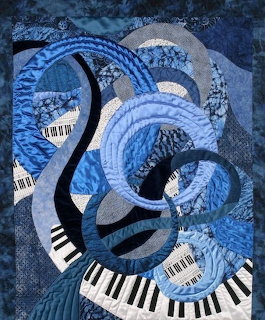 Blue quilted artwork with swirling piano keys and circular fabric patterns in shades of blue and gray