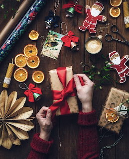 Hands wrapping a Christmas gift on a wooden table with ribbon, dried oranges, and holiday decorations