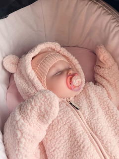 Baby in fluffy pink bear costume with pacifier lying on pink cushioned surface