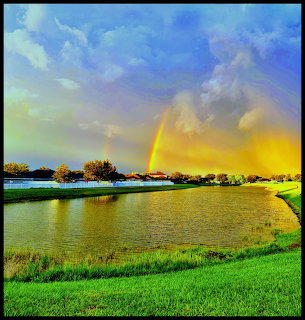 Rainbow over lake with green grass and colorful dramatic sky