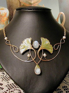 Art Nouveau necklace with green ginkgo leaves, gold wire curves, and white gemstone accents on dark background