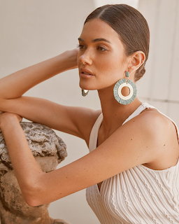 Woman in white striped dress with large circular earrings posing with hand near face