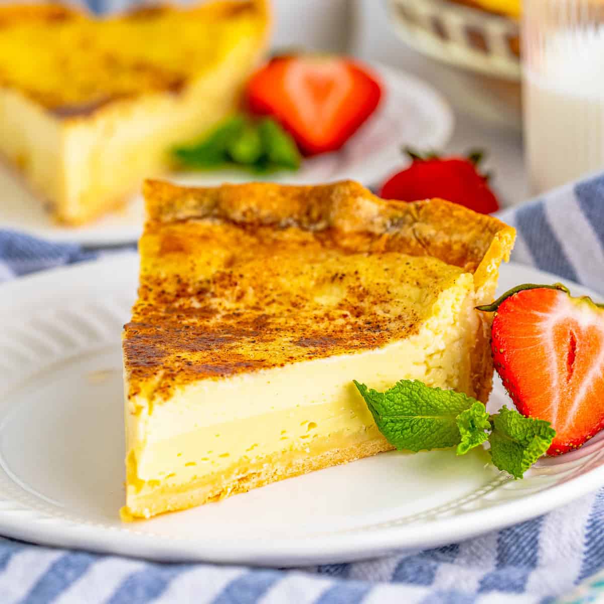 Slice of custard pie with caramelized top, strawberries and mint on white plate