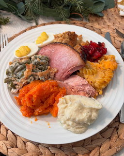 White dinner plate with sliced ham, sweet potatoes, green beans, mashed potatoes, cranberry sauce, and deviled eggs