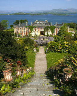 Stone steps leading through terraced gardens to grand historic mansion overlooking blue bay and distant mountains
