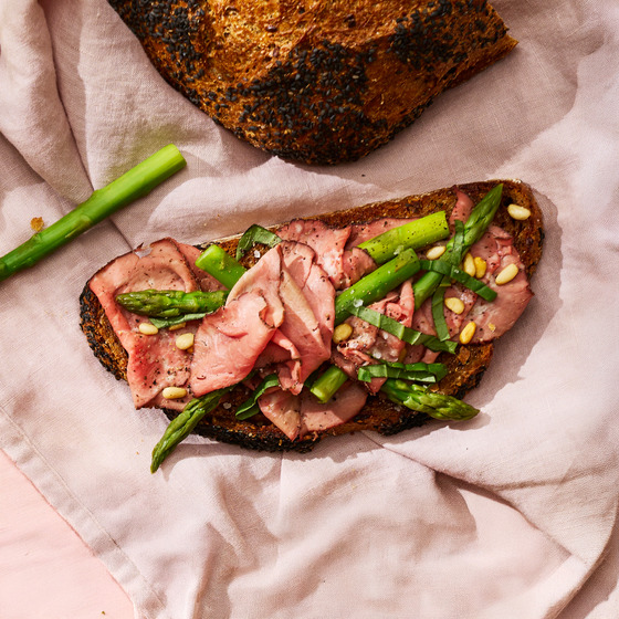 Open-faced roast beef sandwich with green asparagus on dark bread on a pink cloth