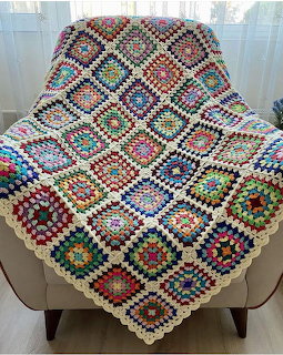 Colorful crocheted granny square blanket with cream scalloped edge draped over a gray chair