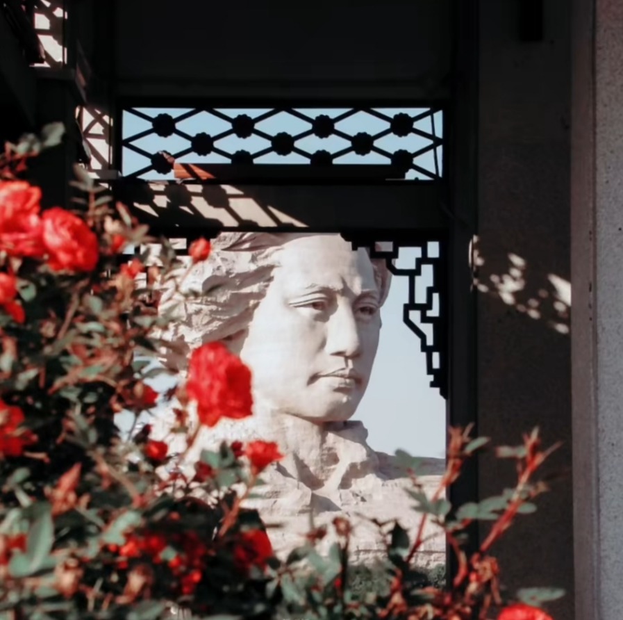 White classical statue framed by a window with red flowers in the foreground