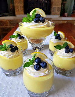 Four glass dessert cups with yellow lemon mousse, whipped cream, blueberries and mint garnish