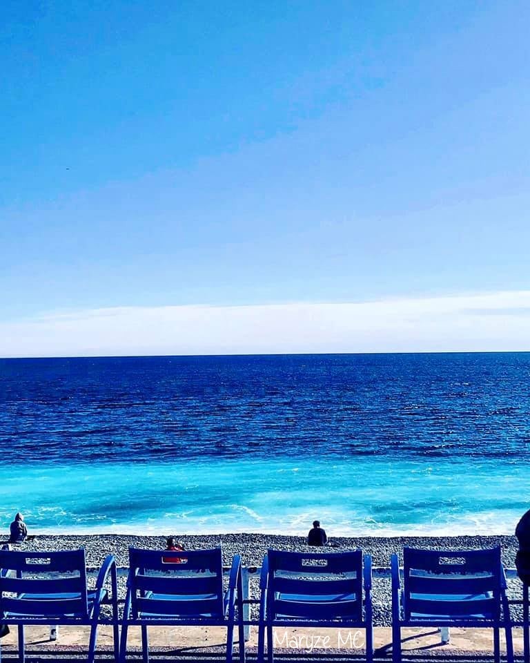 Blue striped beach chairs lined up on pebble beach facing calm turquoise sea and blue sky