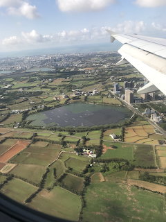 Aerial view from airplane wing showing green fields, a reservoir, and a coastal city in Taiwan