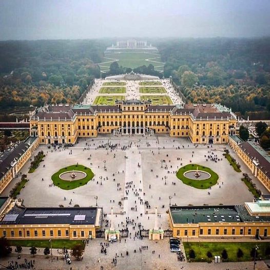 Aerial view of a grand yellow palace with formal gardens and a large courtyard