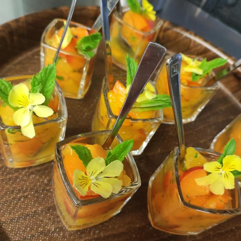 Glass dessert cups with orange puree, mint leaves, yellow flowers, and small spoons