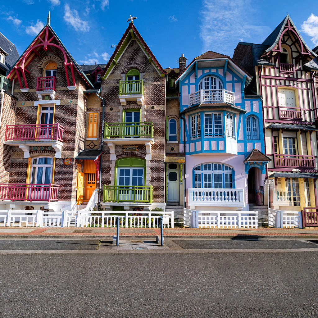 Colorful ornate townhouse facades with balconies and gables along a street under a blue sky