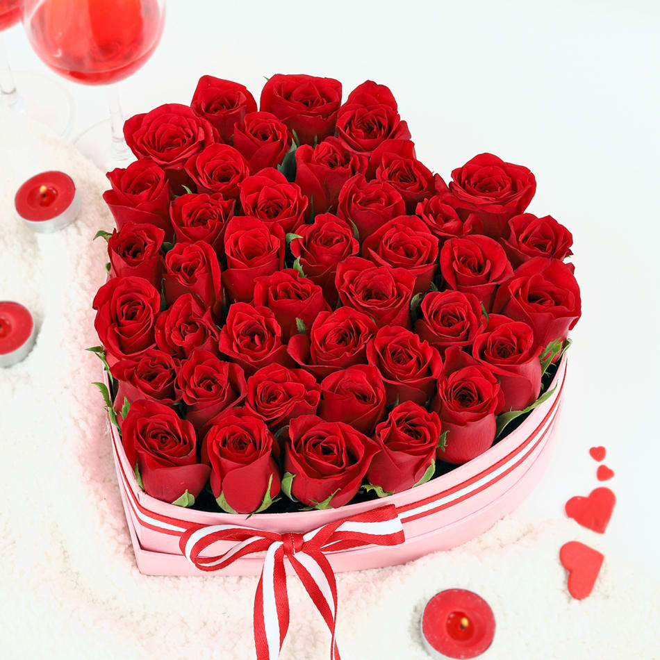 Heart-shaped box of red roses with red candles and heart confetti on a white background