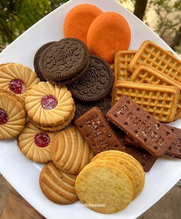 White plate with assorted cookies, biscuits, waffles, and chocolate wafers arranged together