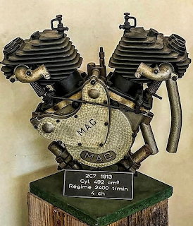 Vintage MAG Motosacoche V-twin motorcycle engine displayed on wooden stand with identification plaque
