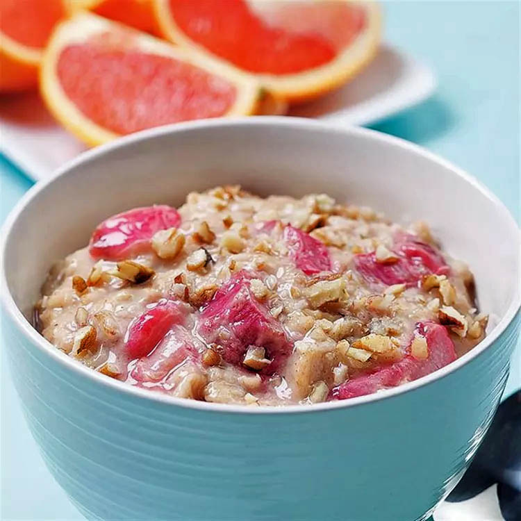 Bowl of oatmeal porridge with pink rhubarb pieces and grapefruit slices behind it