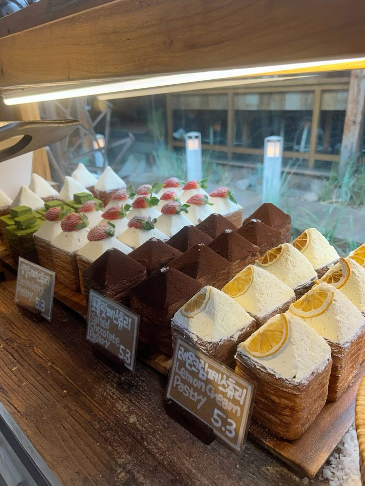 Bakery display case with rows of decorated cake slices including chocolate and cream varieties with fruit toppings