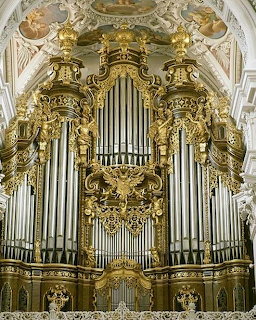 Ornate gilded pipe organ with tall silver pipes in a baroque church interior