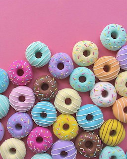 Colorful glazed donuts with sprinkles on pink and purple background