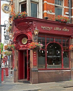 Ornate red corner storefront with flower boxes and large windows on a city street
