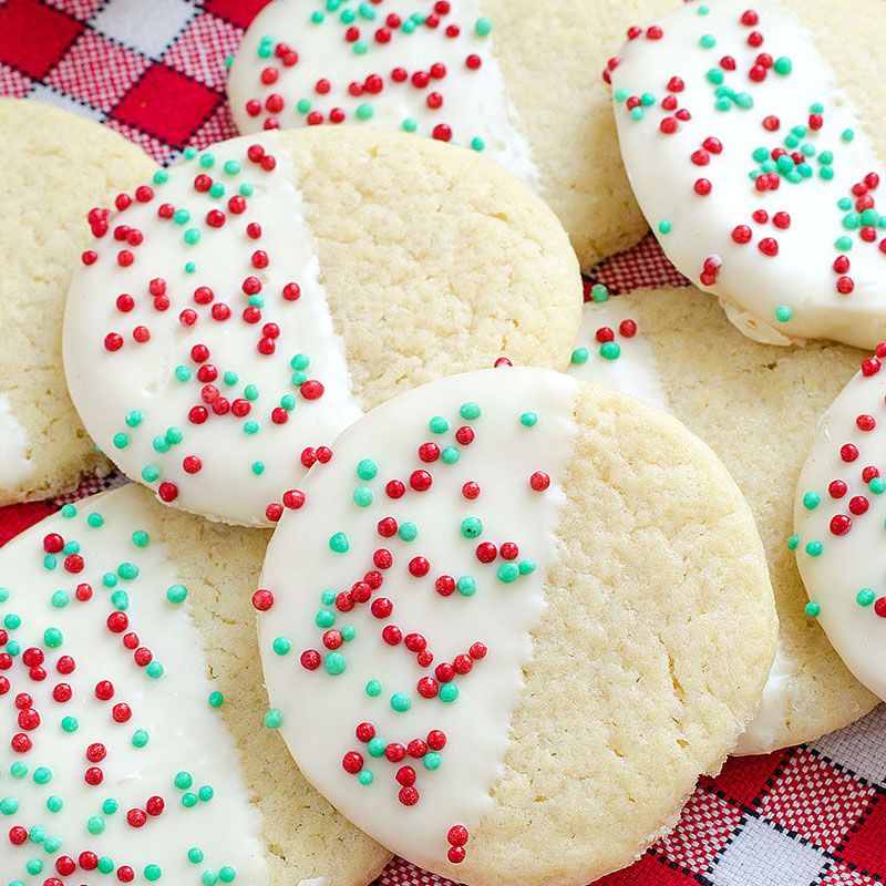 Round sugar cookies with white icing and red and green sprinkles on checkered cloth