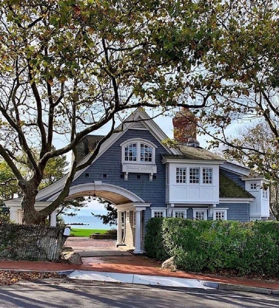 Blue shingle coach house with white trim and arched entrance, surrounded by trees in a coastal New England neighborhood