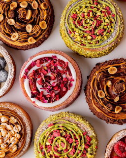 Overhead view of assorted decorative tarts with various toppings including nuts, rose petals, and fruit