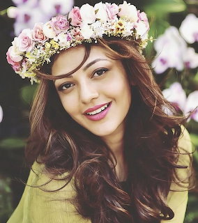 Smiling woman with long brown hair wearing a pink and white flower crown among orchids