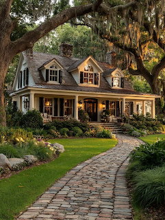 Old house with wraparound porch, large trees, garden, and curved brick path
