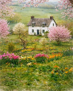 White cottage with blooming pink trees and colorful spring flower garden in front of green hills