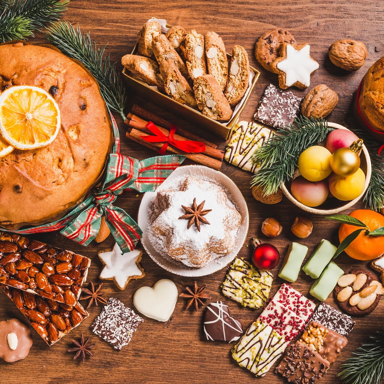 Festive Christmas baked goods and cookies arranged on wooden table with pine branches and ornaments