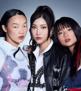 Three women in modern street fashion posing together against blue gradient background